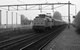 In 1983 rijdt de NS 1221 met een D-trein door Voorschoten. Links zien we het witte pand waar jaren de ANWB verkeersborden werden gemaakt. In 1983 the NS 1221 is passing Voorschoten with a D-train. To the left we see a white building where the ANBW was producing it